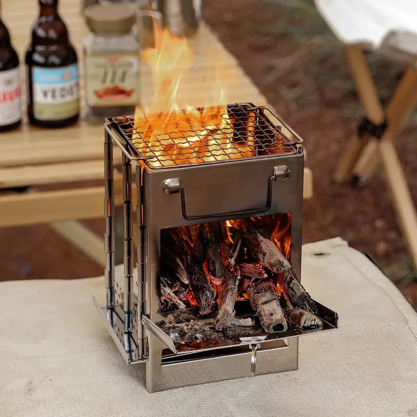 A close up of a small portable grill with a fire burning inside. The grill is made of metal and has a mesh top and a bottom tray for catching ashes. It's sitting on a table with a couple of bottles and a jar behind it. The grill is surrounded by a natural setting, such as a forest or a campsite. The flames are casting a warm glow.