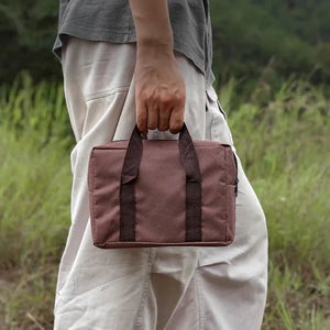 A person wearing white pants and a grey shirt is holding a brown bag. They are standing in a grassy field.